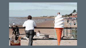 Thumbnail of http://Photo%20of%20man%20standing%20next%20to%20a%20giant%20ice%20cream%20at%20the%20seaside