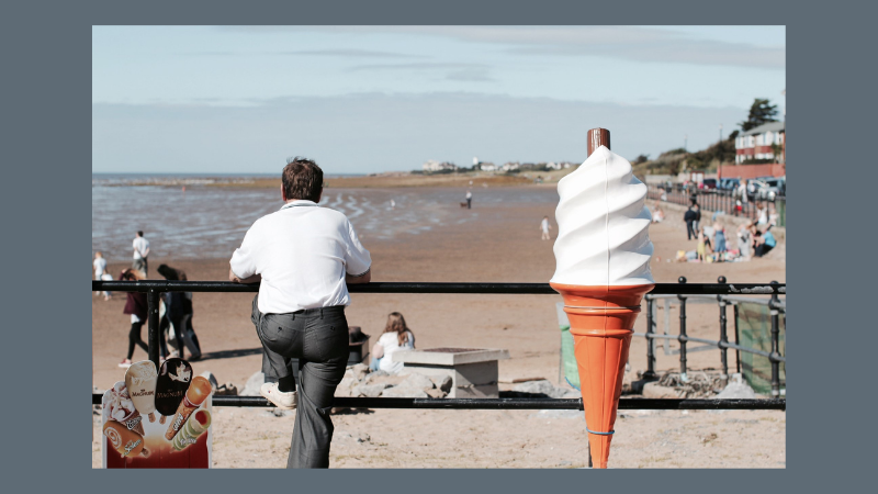 Photo of man standing next to a giant ice cream at the seaside
