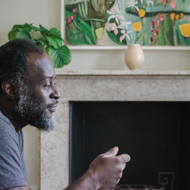 Man sat thinking by a fireplace.