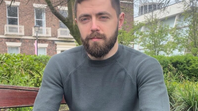 Photo of man with beard sat on a park bench